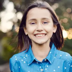 Uśmiechnięta dziewczynka o imieniu Marta, której imię oznacza "pani", w dżinsowej koszuli w białe kwiatuszki.