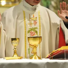 Kapłan w szatach liturgicznych, z podniesionymi rękami, podczas mszy. Na ołtarzu kielichy i księga, symbolizujące credo nicejsko-konstantynopolitańskie.