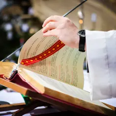 Dłoń kapłana przewraca kartki księgi podczas mszy świętych gregoriańskich.