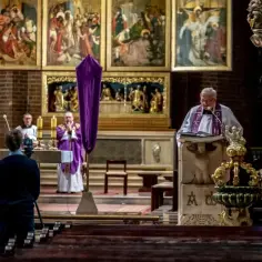 W kościele trwa msza święta, transmitowana przez telewizję. Ksiądz odprawia nabożeństwo, a młody mężczyzna filmuje je kamerą.