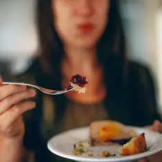 Kobieta bierze widelcem kęs ciasta z dżemem, co może symbolizować nieumiarkowanie w jedzeniu i piciu.