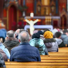 Ludzie siedzący w kościele na drewnianych ławkach, widok zza pleców.