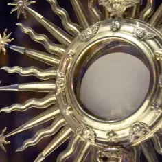 Złota monstrancja z hostią, symbol wystawienia Najświętszego Sakramentu, ozdobiona aniołkami i promieniami.