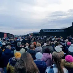 Tłum ludzi uczestniczy w Drodze Krzyżowej na Majdanku, wśród historycznych baraków obozu.