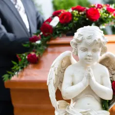 Aniołek z różą obok trumny, symbolizujący obrzędy pogrzebu. W tle mężczyzna w garniturze.