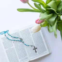 Błękitny różaniec na otwartej Biblii, symbol listu Boga do człowieka. Obok bukiet tulipanów.