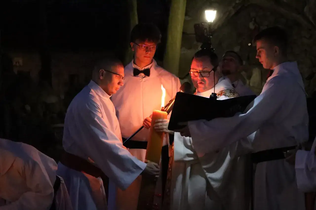 Uroczysta msza święta wielkanocna. Kapłan i ministranci przy zapalonej paschalnej świecy.