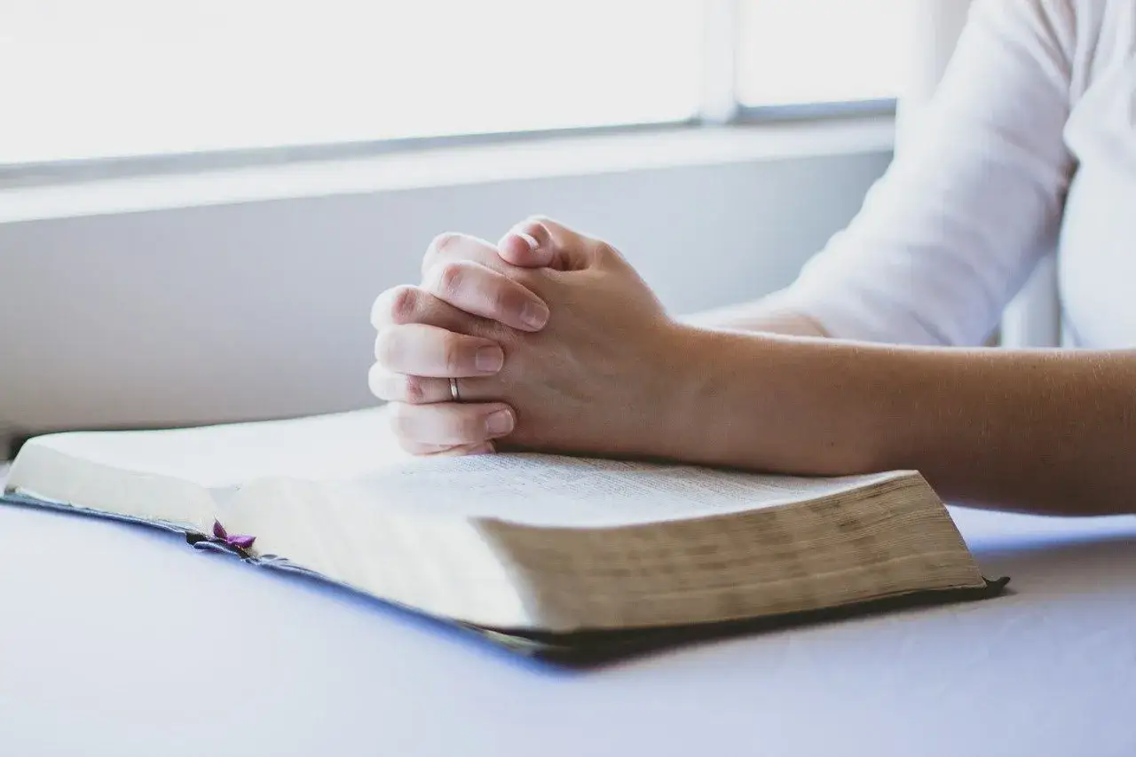 Dłonie złożone w modlitwie nad otwartą Biblią, symbolizujące akt żalu za grzechy i poszukiwanie przebaczenia.