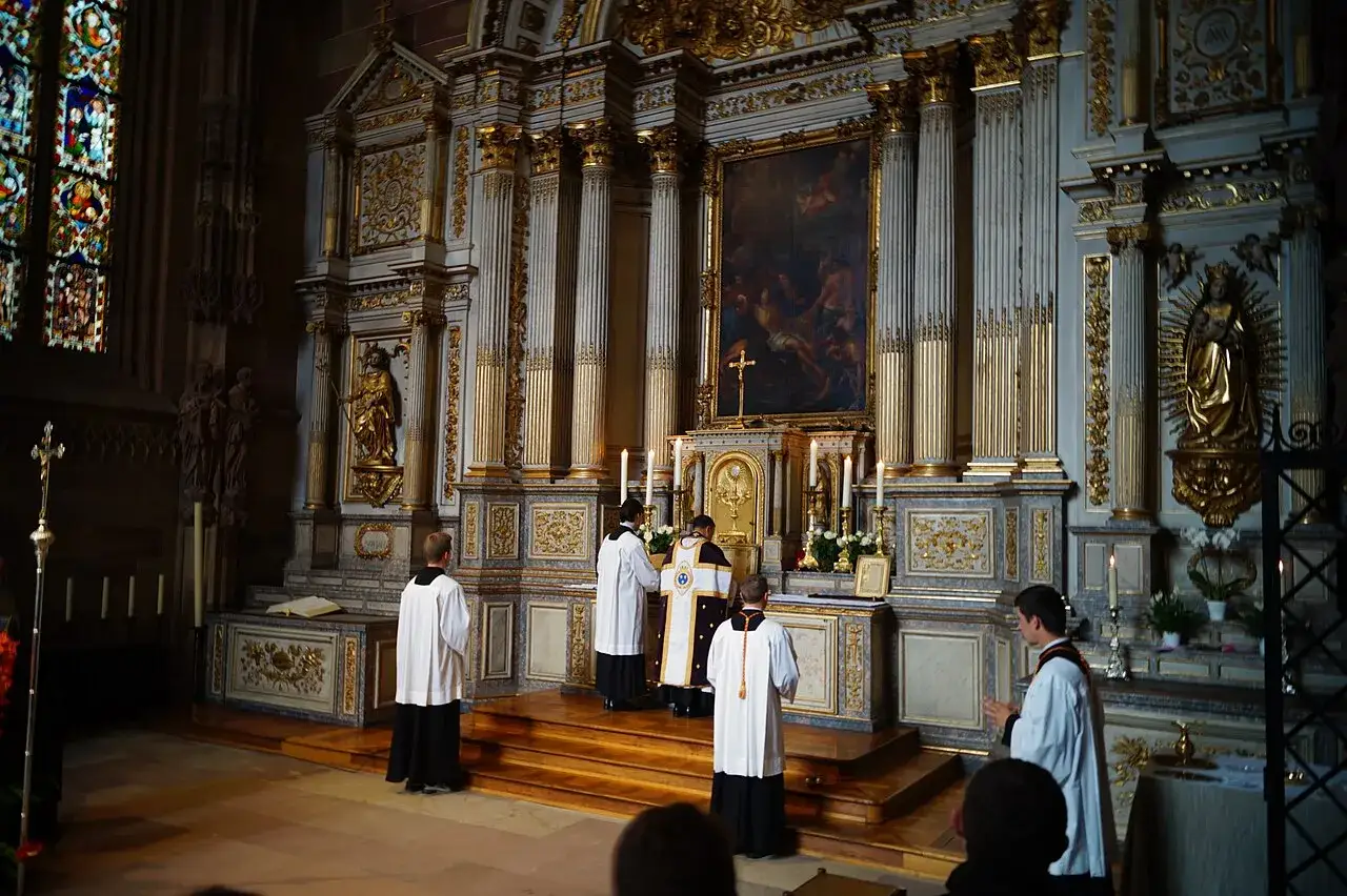 Uroczysta msza w kościele. Klerycy w albach i sutannach przygotowują się do liturgii. W tle ołtarz z obrazem i świecami. Tekst kanonu rzymskiego jest częścią tej świętej ceremonii.