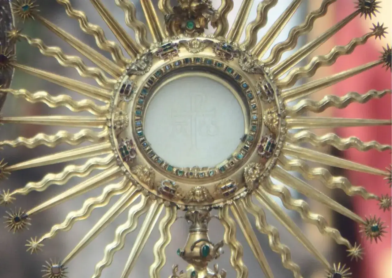 Złota monstrancja z hostią, symbolizująca wystawienie Najświętszego Sakramentu, ozdobiona klejnotami i promieniami.