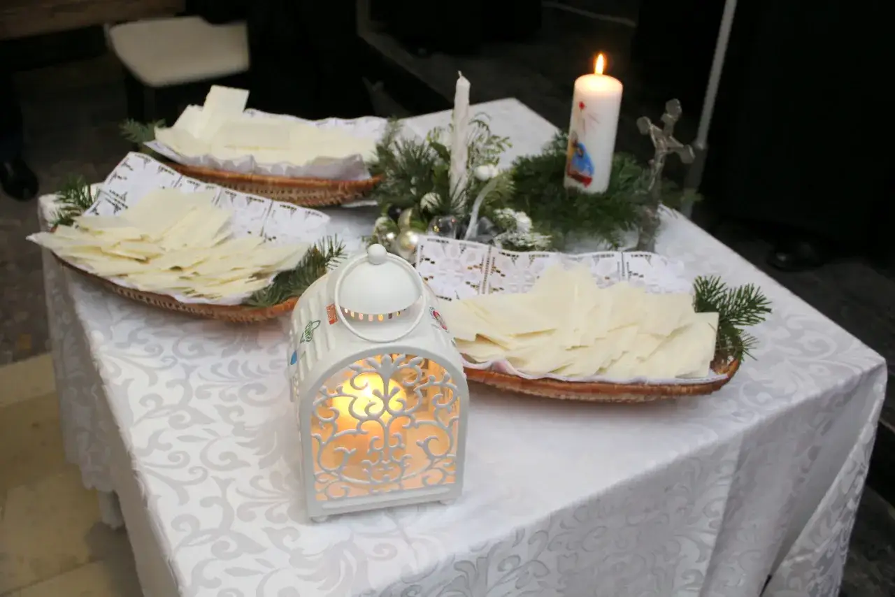 Świąteczny stół z opłatkami i świecą, gotowy do modlitwy przed wieczerzą wigilijną.