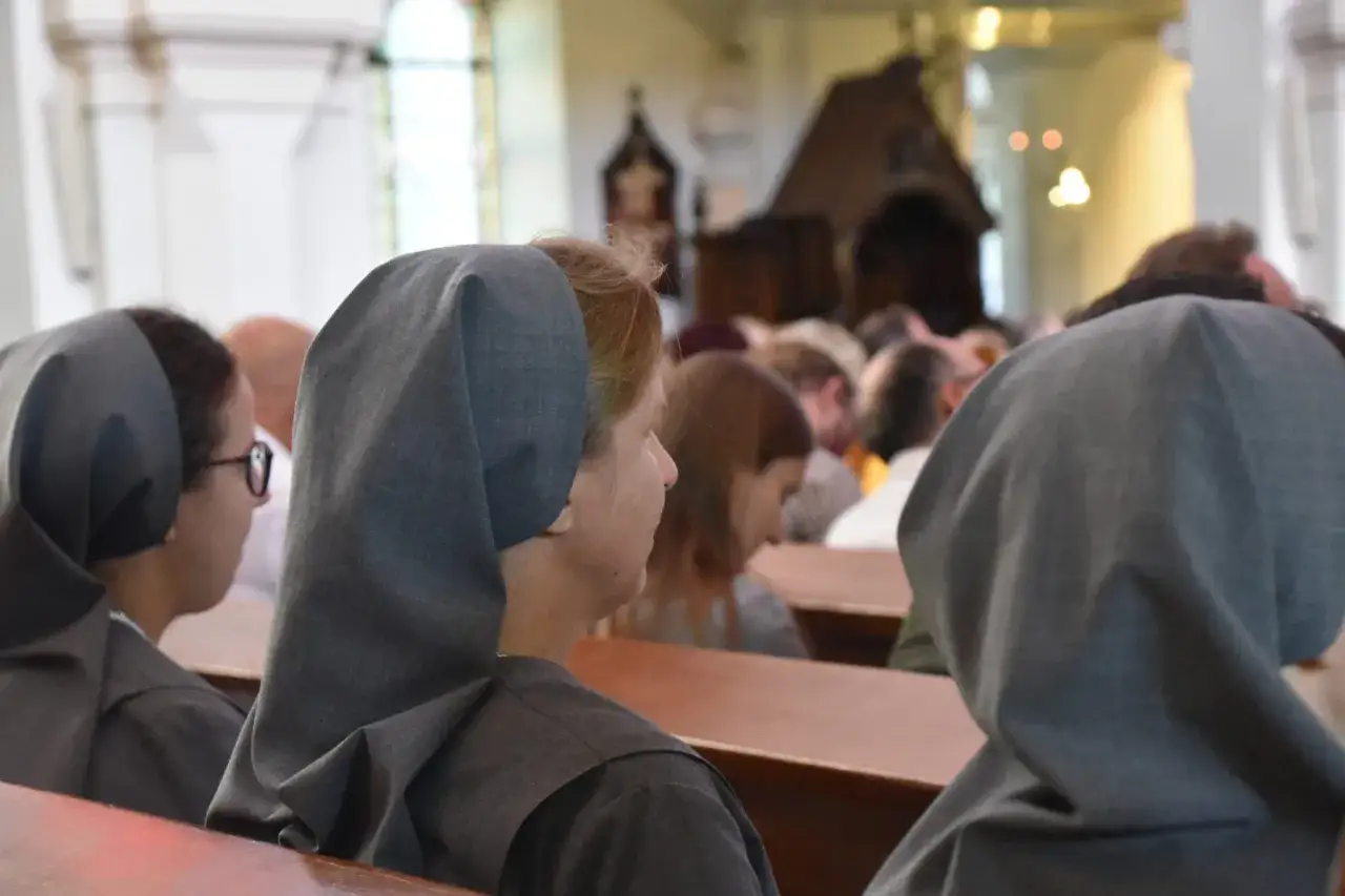 Siostry zakonne w szarych habitach siedzą w kościele, celebrując dzień życia konsekrowanego.