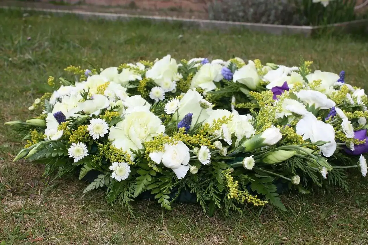 Wieniec pogrzebowy z białych kwiatów i zieleni, symbol pamięci i szacunku podczas obrzędów pogrzebu.