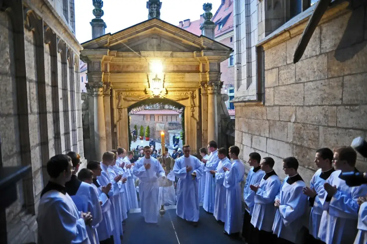 Uroczysta msza święta wielkanocna. Klerycy w białych albach wychodzą z kościoła, niosąc paschał.